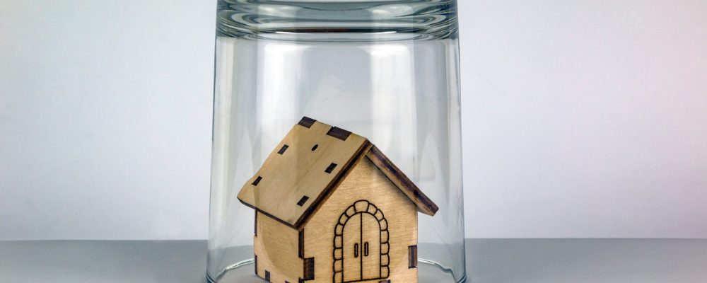 Wooden model of a house under a glass cover on a white background.
